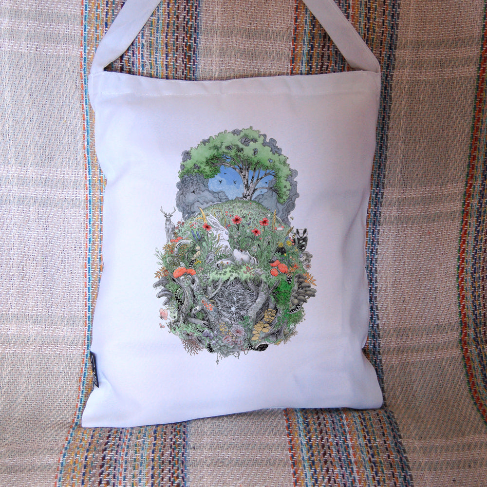 A roughly oval design, topped with a tree in full leaf, surrounded by clouds, but clearing to blue in the centre, and swifts wheeling all around. Beneath, the top half of the oval is a flower-filled meadow. A stag and badger stand either side, and a hare, blackbird, mouse, and other creatures are nestled within. The head and shoulders of a young woman lying on her back rise from the ground. Beneath her, the bottom half of the oval is a mass of twisting roots, branches, leaves, fungi and toadstools ...