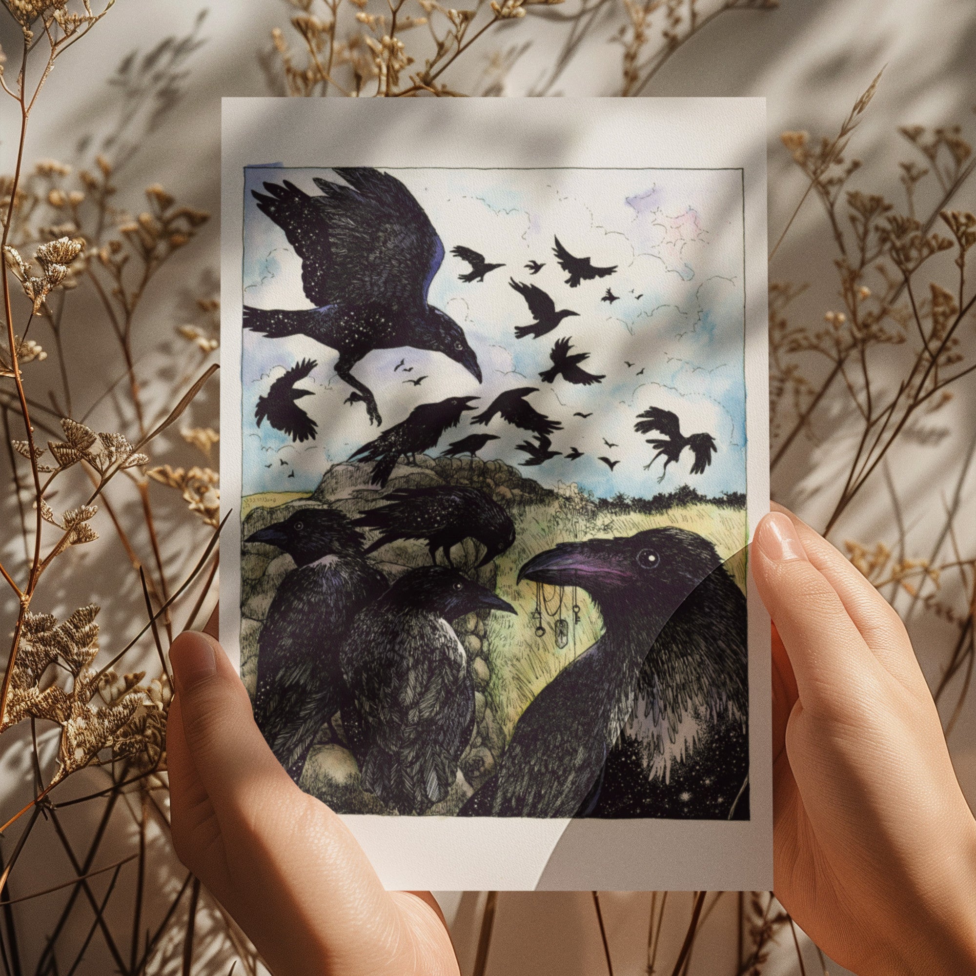 Person holding a card with raven illustration surrounded by dried plants