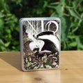 The head and chest of a badger, head turned sideways, rises up from behind an array of mushrooms, moss and berried holly. The mushrooms flow up the trunk of an ancient tree; a face appears from the mossy bark. Another badger approaches from behind. Tall, bare tree trunks stand in the distance, and a crescent moon shines above. The badgers and background scene are mostly black and white, the plants and trees are shades of green and dusky pink.