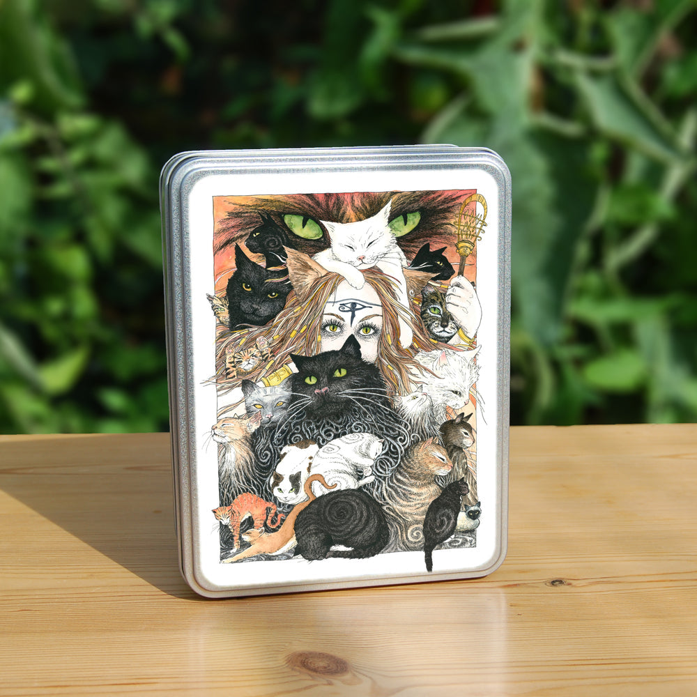 A mass of cats of all colours and in many poses surrounds the face of a red-haired woman with cat-slit eyes and ears, and a Eye of Horus symbol on her forehead. A white cat sits on her head. She holds a gold-coloured sistrum (a type of rattle) in one hand. The head of a much larger cat with green eyes appears above and behind them. Colours are oranges, reds, black and white.