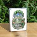 A roughly oval design, topped with a tree in full leaf, surrounded by clouds, but clearing to blue in the centre, and swifts wheeling all around. Beneath, the top half of the oval is a flower-filled meadow. A stag and badger stand either side, and a hare, blackbird, mouse, and other creatures are nestled within. The head and shoulders of a young woman lying on her back rise from the ground. Beneath her, the bottom half of the oval is a mass of twisting roots, branches, leaves, fungi and toadstools ...