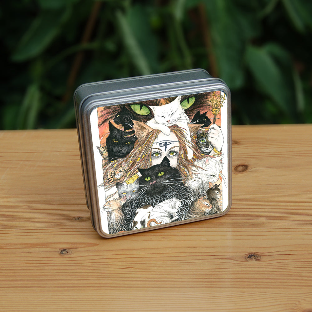 A mass of cats of all colours and in many poses surrounds the face of a red-haired woman with cat-slit eyes and ears, and a Eye of Horus symbol on her forehead. A white cat sits on her head. She holds a gold-coloured sistrum (a type of rattle) in one hand. The head of a much larger cat with green eyes appears above and behind them. Colours are oranges, reds, black and white.