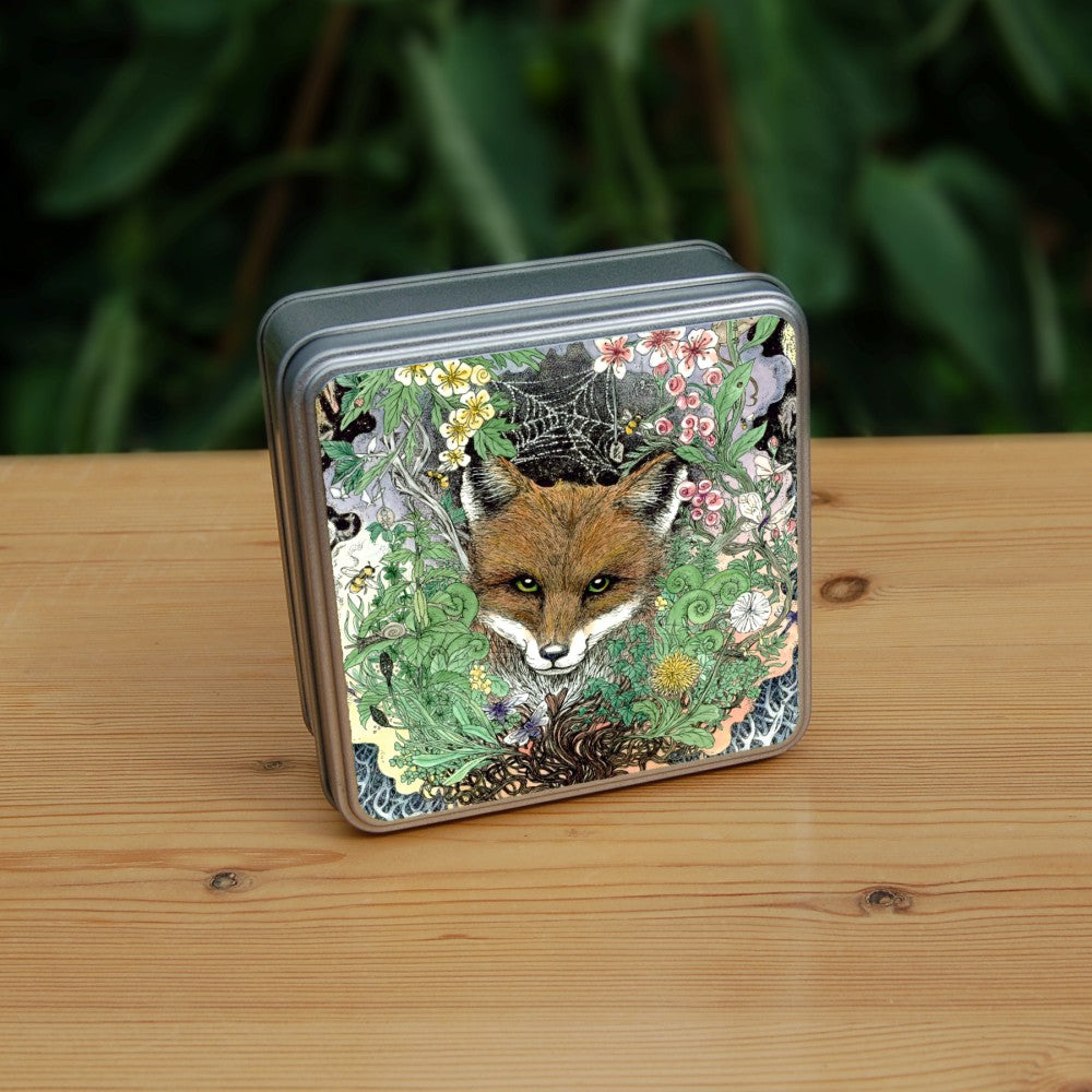 The head of a red fox looks towards the viewer. He's surrounded by a mass of leaves and flowers which rise out from a twisted tree trunk and tangled branches.