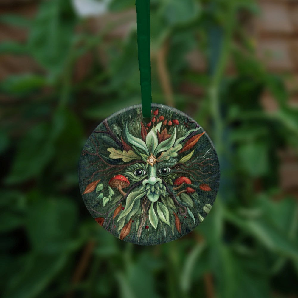 A pair of green eyes, with prominent nose beneath, is surrounded by red and green leaves radiating out from the central face. Red toadstools grow out from his cheeks and the top of his head. Two delicate tree branches protrude like antlers. The background is dark green.