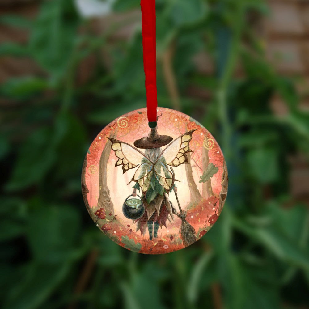 The rear view of a fairy walking in enchanted woodland. She has brown and white butterfly wings, and wears a pointed brown hat and green and brown dress. In her left hand she carries a cauldron, and in her right, a traditional broomstick. The woodland is cast in reds. Red and white toadstools grow on both sides, oak leaves tumble towards the ground, and faces can be seen in the trees.