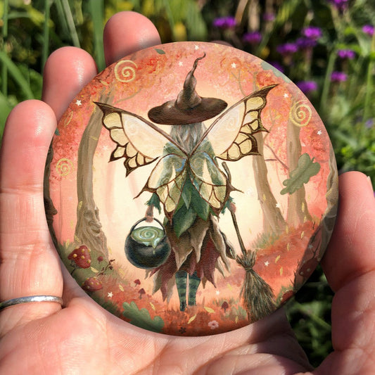 The rear view of a fairy walking in enchanted woodland. She has brown and white butterfly wings, and wears a pointed brown hat and green and brown dress. In her left hand she carries a cauldron, and in her right, a traditional broomstick. The woodland is cast in reds. Red and white toadstools grow on both sides, oak leaves tumble towards the ground, and faces can be seen in the trees.