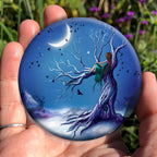 A girl with long red hair and wearing a deep green dress, sits in the branch of a leafless tree, looking away from the viewer into the distance. There's snow on the tree and the ground. The tree has a twisted trunk with a small door at the bottom. A crescent moon shines over a starlit midnight blue sky. Birds fly in every direction, a barn owl hunts beneath the tree, and ghostly silhouettes of a stag, hare and running fox can be seen. Colours are rich blues and purples.