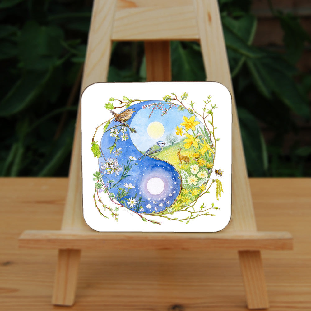 A Yin-Yang shape is surrounded by sprouting branches of native trees. The left hand half of the shape is filled with blue sky, and a large, watery sun forms the traditional 'dot'. White blossom and spring flowers overlay the sky, and a wren sings from a branch at the top. The right hand half features a hare sitting in a grassy field in a sunny day. A pale yellow sun forms the 'dot'. Yellow flowers overlay the scene. A blue tit sits on a branch forming the curve between the two sections.