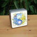 A Yin-Yang shape is surrounded by sprouting branches of native trees. The left hand half of the shape is filled with blue sky, and a large, watery sun forms the traditional 'dot'. White blossom and spring flowers overlay the sky, and a wren sings from a branch at the top. The right hand half features a hare sitting in a grassy field in a sunny day. A pale yellow sun forms the 'dot'. Yellow flowers overlay the scene. A blue tit sits on a branch forming the curve between the two sections.