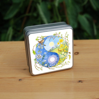 A Yin-Yang shape is surrounded by sprouting branches of native trees. The left hand half of the shape is filled with blue sky, and a large, watery sun forms the traditional 'dot'. White blossom and spring flowers overlay the sky, and a wren sings from a branch at the top. The right hand half features a hare sitting in a grassy field in a sunny day. A pale yellow sun forms the 'dot'. Yellow flowers overlay the scene. A blue tit sits on a branch forming the curve between the two sections.