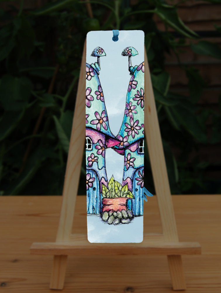 Half of two pink and blue / green toadstool houses standing in a row. The roofs and walls are liberally decorated with simple flower designs have curved windows and have curved blue front doors. Tiny toadstool-shaped chimney pots protrude from each roof, and red planters surrounded by stones and with leafy plants growing from each sit between each house. The background is a mottled pale blue.