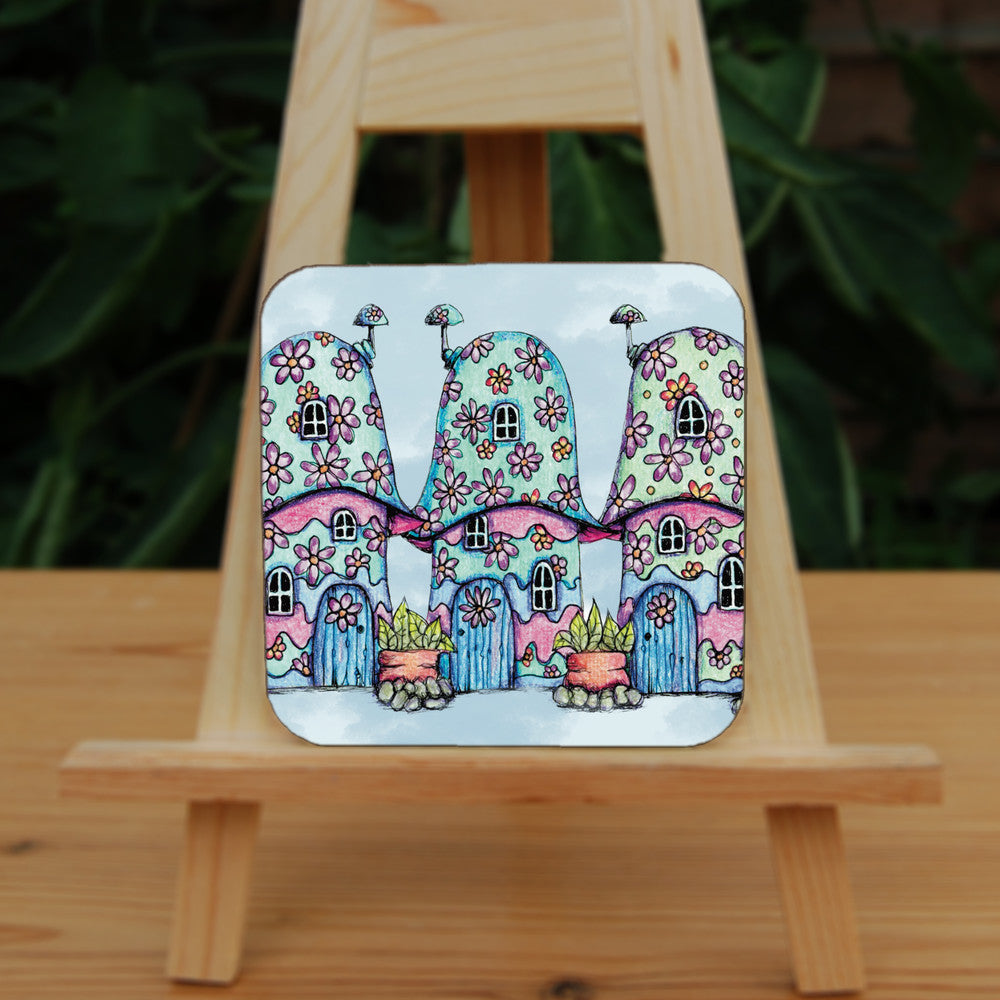 Three pink and blue / green toadstool houses stand in a row. The roofs and walls of all four are liberally decorated with simple flower designs have curved windows (two stories, plus a window in the roof) and have curved blue front doors. Tiny toadstool-shaped chimney pots protrude from each roof, and red planters surrounded by stones and with leafy plants growing from each sit between each house. The background is a mottled pale blue.