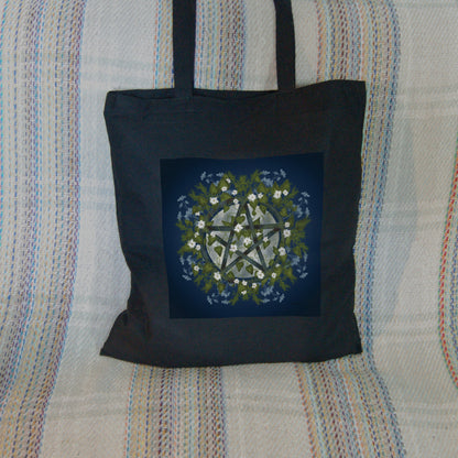 A pentacle symbol overlaid with green leaves, foliage and white flowers which extend outwards towards the edge of the design. A silvery full moon shines behind and within the circle of the pentacle. The background is deep blue.