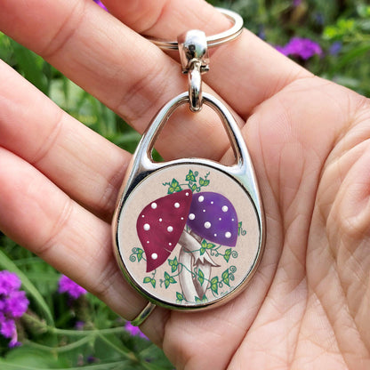 Two toadstools with long pale stems are twined together. The cap of one of them is red with white spots, the other purple with white spots. Leafy green tendrils twine around and up the pair. The background is a mottled beige colour.