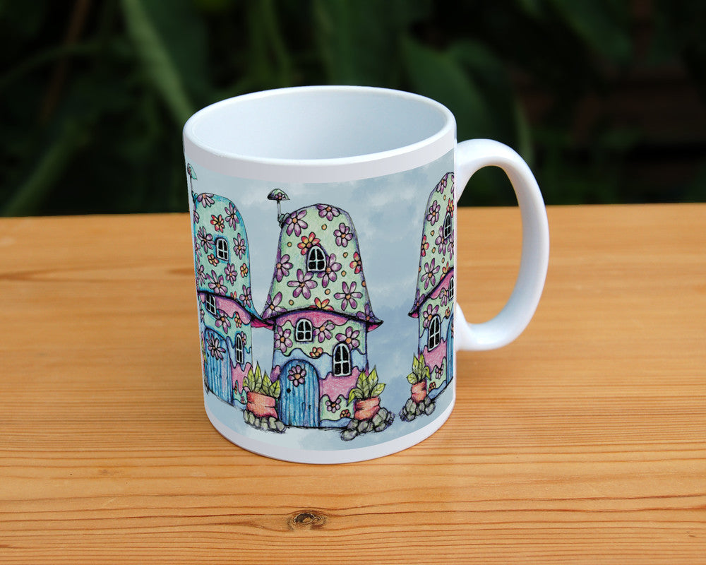 Four pink and blue / green toadstool houses stand in a row. The roofs and walls of all four are liberally decorated with simple flower designs have curved windows (two stories, plus a window in the roof) and have curved blue front doors. Tiny toadstool-shaped chimney pots protrude from each roof, and red planters surrounded by stones and with leafy plants growing from each sit between each house. The background is a mottled pale blue.