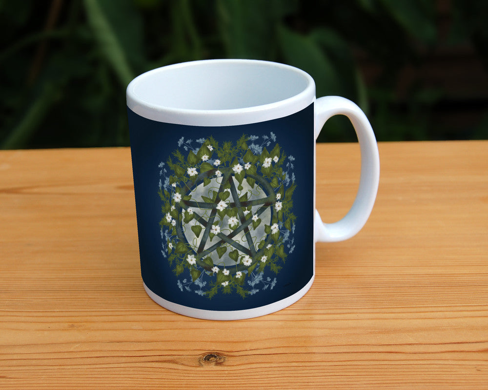 A pentacle symbol overlaid with green leaves, foliage and white flowers which extend outwards towards the edge of the design. A silvery full moon shines behind and within the circle of the pentacle. The background is deep blue.