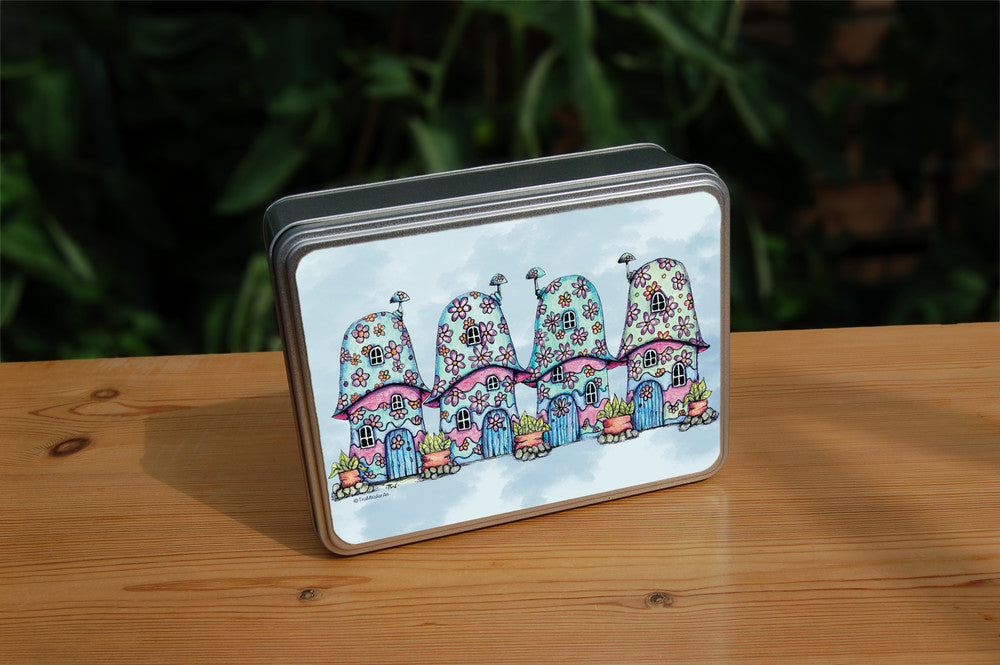 Four pink and blue / green toadstool houses stand in a row. The roofs and walls of all four are liberally decorated with simple flower designs have curved windows (two stories, plus a window in the roof) and have curved blue front doors. Tiny toadstool-shaped chimney pots protrude from each roof, and red planters surrounded by stones and with leafy plants growing from each sit between each house. The background is a mottled pale blue.