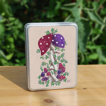 Two toadstools with long pale stems are twined together. The cap of one of them is red with white spots, the other purple with white spots. More small toadstools are dotted around the foot of the pair, and leafy green tendrils twine around and up the main pair. The background is a mottled beige colour.