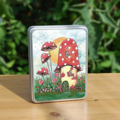 A cream toadstool house with red and white spotted roof, white curved windows, and an oval green door at the bottom. A low stone wall, entwined with leaves and red flowers, extends to each side, behind which is a mass of tall plants, several tall red toadstools on thin stems. An orange sun rises behind the house against a pale cloudy sky, and a flock of birds flies by.