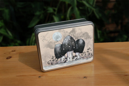 A cluster of toadstools with black caps. The cap of the centre toadstool has white spots. They're surrounded by the silhouettes of leafy plants, and a mist lies low on the ground. Above them a silvery full moon shines, and a flock of birds flies across. The background is a mottled beige.