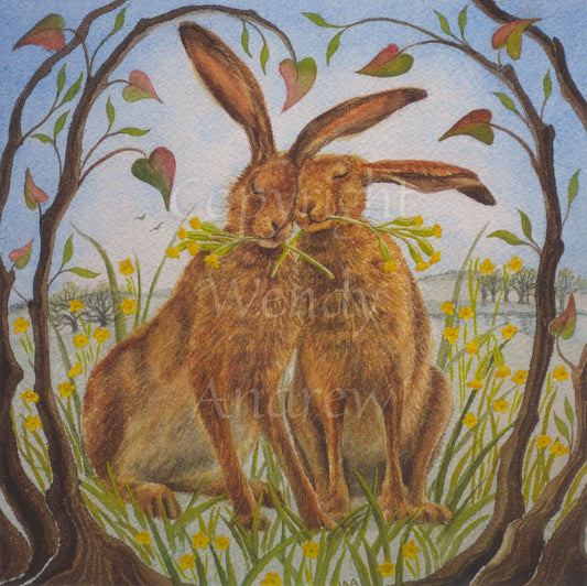 Two brown hares lean towards each other, eyes closed, heads touching, holding flowering stems of cowslip in their mouths. Branches with newly-formed leaves form an arch over them. They’re surrounded by cowslips in flower, with fields and blue skies in the background.